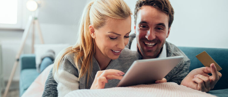 Mann und Frau liegen auf einem bett und schauen sich fröhlich Sachen auf ihrem Ipad an
