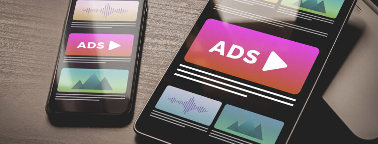 Zwei Smartphones auf einer Tischoberfläche, beide zeigen Anzeigen mit dem Text "ADS" und verschiedenen grafischen Elementen.